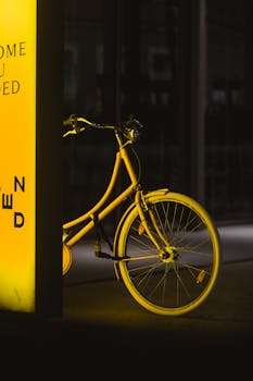 A sleek yellow bicycle glowing under city lights creates a serene urban night scene.
