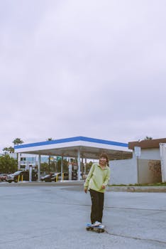 Joyful woman skateboarding near a gas station in Chula Vista, CA on a cloudy day.