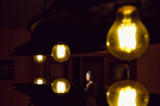A bride poses elegantly in dramatic lighting surrounded by glowing bulbs, creating a unique wedding portrait.