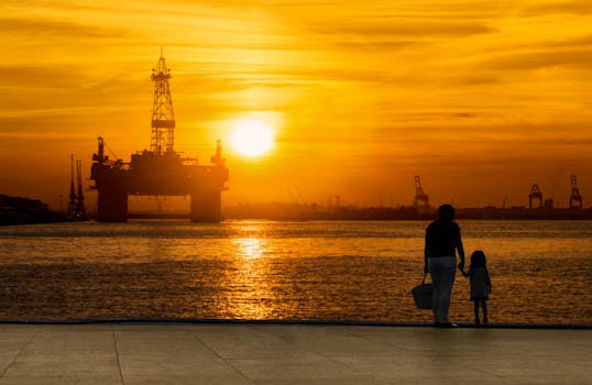A heartwarming silhouette of a parent and child holding hands at sunset by an oil rig in Rio de Janeiro.