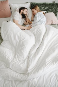 A serene moment of a couple sleeping in a cozy bedroom with white bedding.