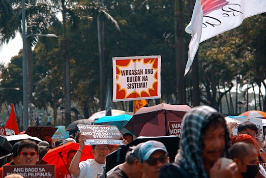 Crowded protest in Manila with colorful signs and umbrellas under a sunny sky, conveying a sense of activism.