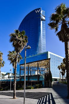 The W Hotel in Barcelona amidst palm trees on a sunny day, showcasing modern architecture.